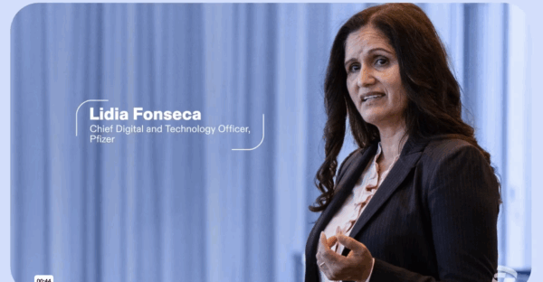 A woman in business attire, identified as Lidia Fonseca, Chief Digital and Technology Officer at Pfizer, stands and gestures while speaking in front of a blurred blue background.